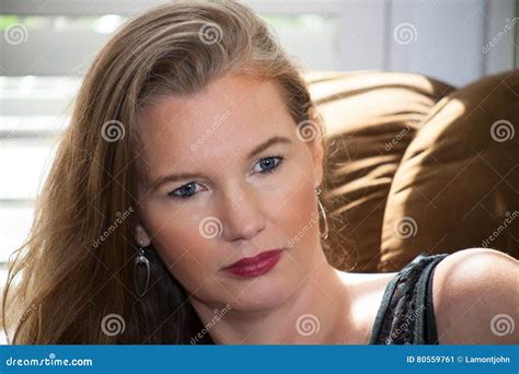 Closeup Mature Blonde Female Sitting On Sofa In Front Of Window Stock