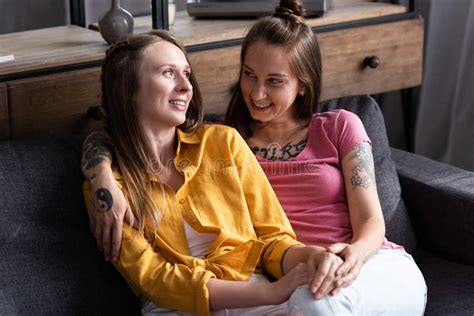 Two Pretty Lesbians Embracing While Sitting On Sofa In Living Room