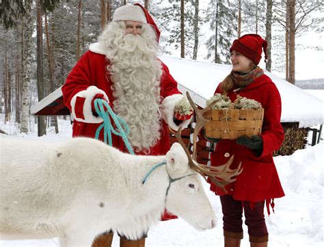 photo santa claus and elf feeding a reindeer in lapland finland