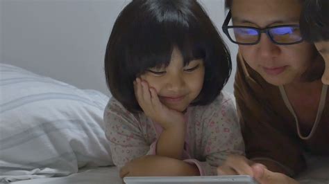 asian mom lies with her daughters and plays with digital tablet