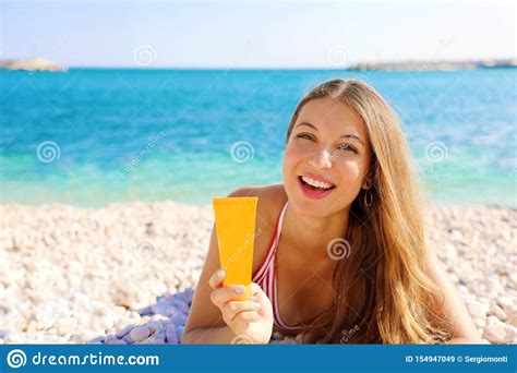 smiling woman holding sun cream tube protection lying on pebbles beach