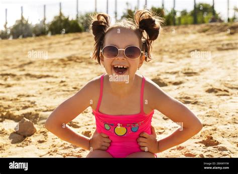 a beautiful girl in a pink swimsuit and glasses is sitting on a sandy