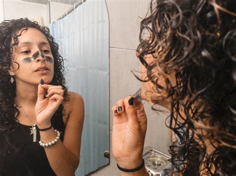 woman peeling off black facial mask of her face in the bathroom stock