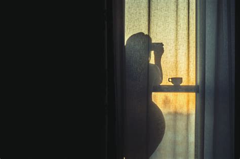 A Naked Girl Is Standing By The Window Behind The Curtain And Drinking
