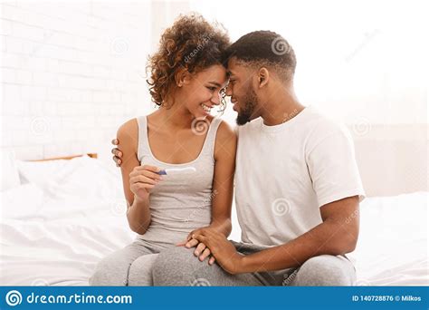 Happy Couple Holding Positive Pregnancy Test On Bed Stock