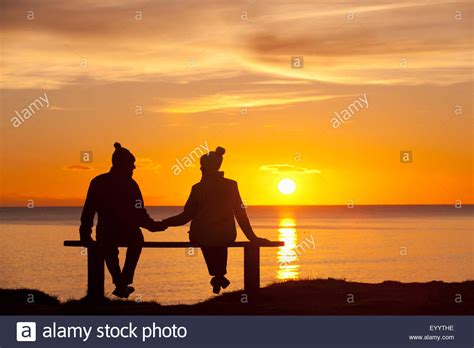 Silhouette Of Couple Sitting On Bench Holding Hands