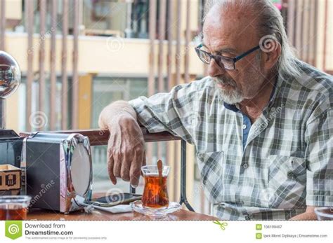 Old Turkish Man With Eyeglasses Looking At His Smartpone While Drinking