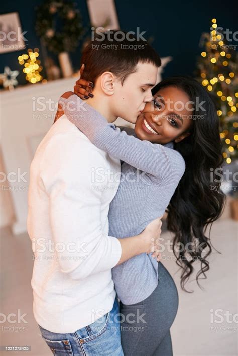 크리스마스 밤에 거실에서 껴안고 있는 아름다운 흑인 소녀와 백인 남자 인종 간 관계 사랑에 빠진 신혼 부부 새해 축하 로맨스에