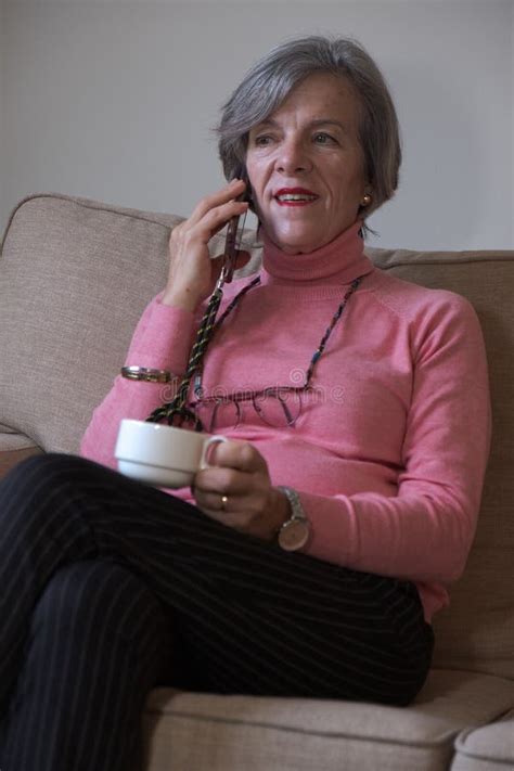 Happy Mature Woman Talking Cell Phone While Sitting On Sofa Having