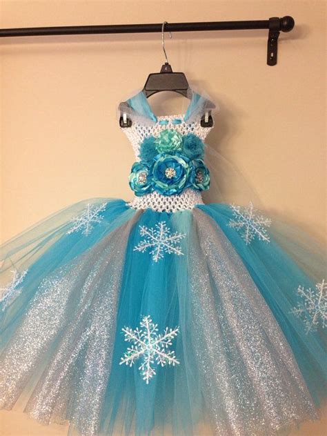 a blue and white dress with snowflakes hanging on a rack in front of a wall