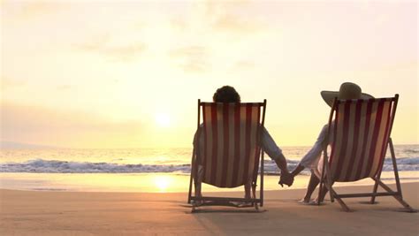 Romantic Couple Sitting In Wooden Deckchairs On The Beach