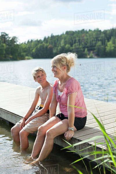 Happy Mature Woman Sitting With Son On Pier During Vacations Stock