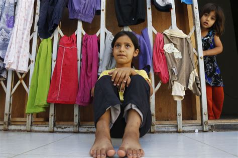 a syrian refugee girl sits in front of hanging clothes as another girl