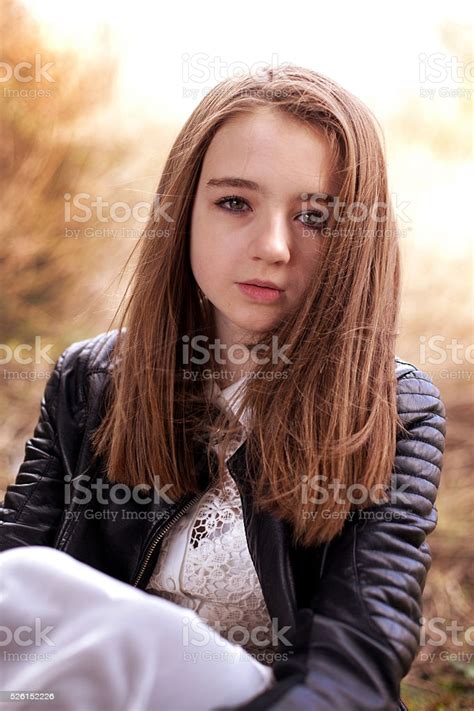 pretty teenage girl sitting outdoors looking straight to camera stock