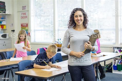 Ethnic Female Elementary Teacher Posing In Front Of Classroom Stock
