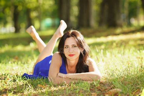 Beautiful Young Woman Smiling In Blue Dress Lying On The Grass Stock
