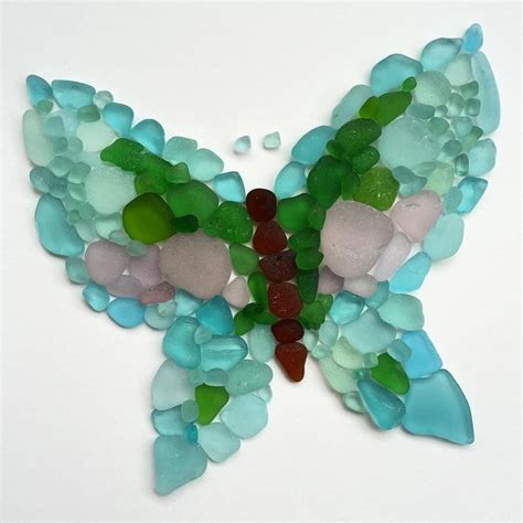 A Butterfly Made Out Of Sea Glass Sitting On Top Of A White Table Next