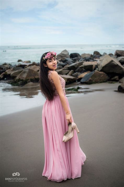 A Woman Standing On Top Of A Beach Next To The Ocean Wearing A Pink Dress