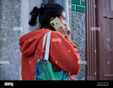 A Young Spanish Girl In An Orange Hoodie Talking On The Phone Outside