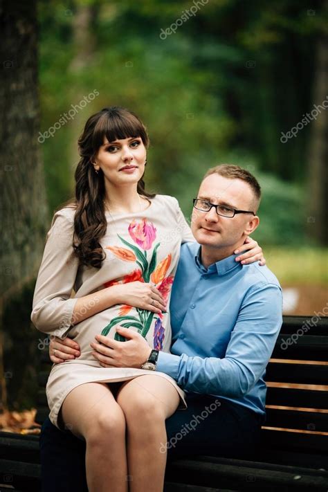 beautiful and happy pregnant couple relaxing outside in the autumn park sitting on bench