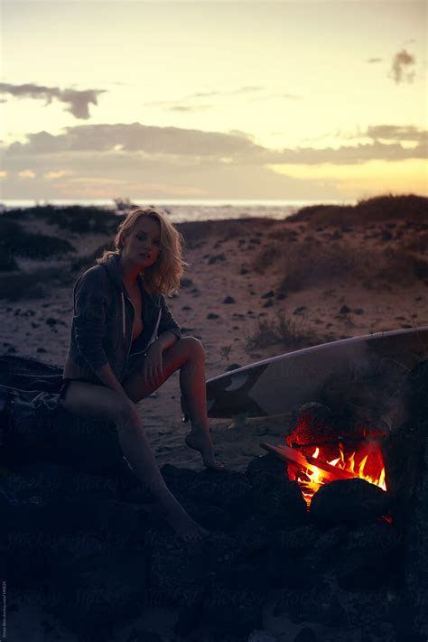 Female Blonde Surfer Sitting At Fireplace On The Beach By Simon Bolz