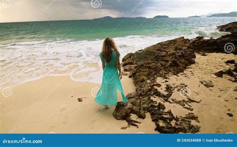 woman walks to the stormy cloudy ocean on sand beach girl in blue