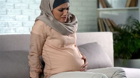 gelukkige zwangere vrouw  hijab wat betreft buik die zacht huis prenatale zorg rusten stock