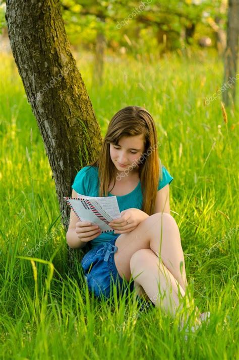 beautiful teenage girl reading letter while sitting under