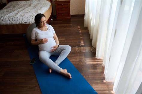 Pregnant Woman Sitting Barefoot On Yoga Mat Stroking Her Big Belly