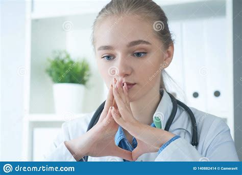 Young Serious Blonde Doctor Woman Sitting In Medical Office With Hands