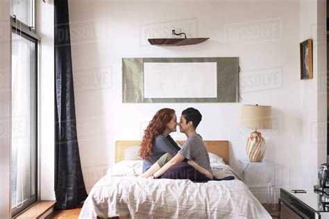 Side View Of Romantic Lesbians Rubbing Noses While Sitting On Bed