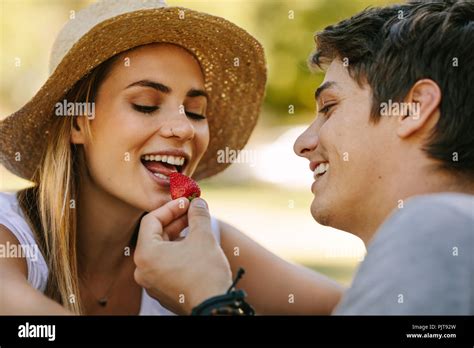 man feeding his girlfriend with a strawberry sitting outdoors woman