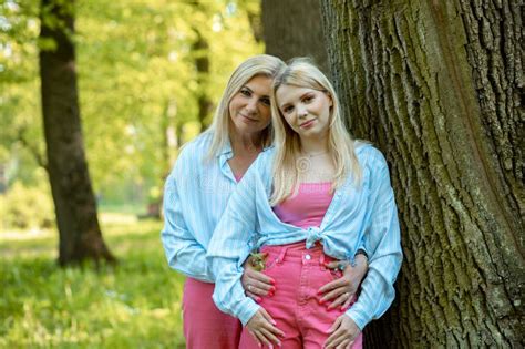 Two Smiling Blonde Mom And Daughter Dressed Identically Are Standing