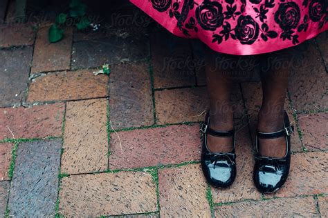 black girl s feet in patent leather shoes and pink dress by stocksy