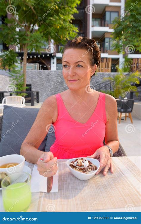 Mature Scandinavian Tourist Woman Having Breakfast Outdoors In Resort