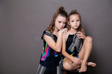 Portrait Of Two Beautiful Fashionable Sisters Girls On A Gray