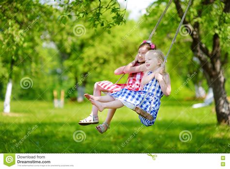Two Cute Little Sisters Having Fun On A Swing Together In Beautiful