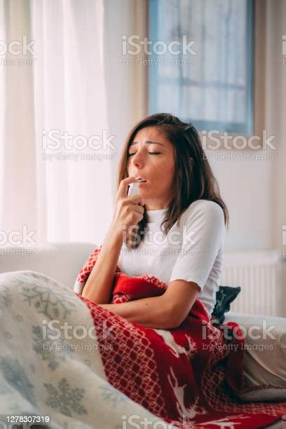 Sick Woman Lying On The Sofa Spraying A Medication Into Her Throat
