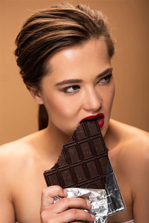 ベージュに隔離された銀箔でチョコレートバーを噛む赤い唇を持つ美しい裸の女性 ロイヤリティフリー写真・画像素材