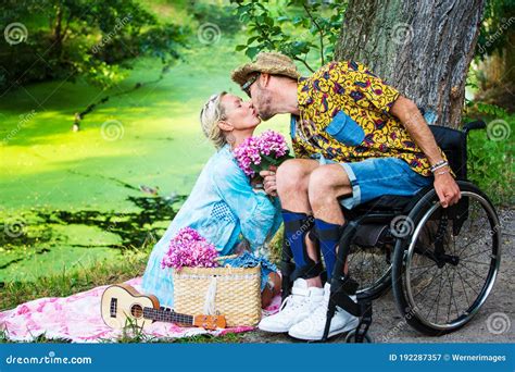 Man In Wheelchair Kissing Blond Woman Sitting By River Stock Image