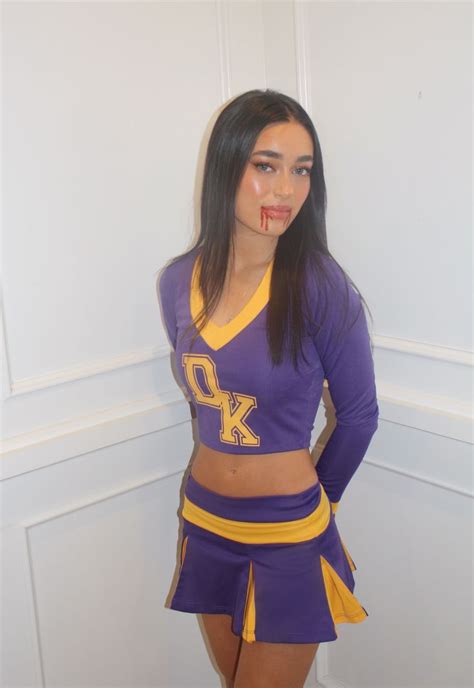 A Woman In A Purple And Yellow Cheerleader Outfit Posing For The Camera