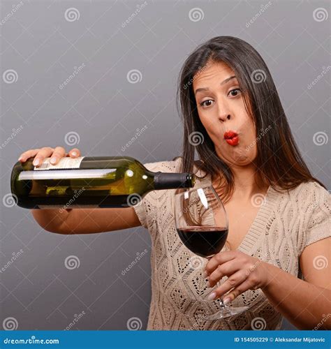 Portrait Of Woman Holding Wine Bottle And Glass Against Gray Background