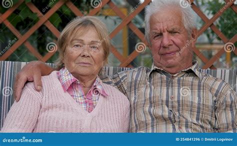 Portrait Elderly Couple Sitting On Swing In Garden Hugging Stock
