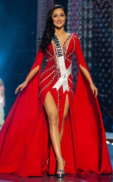 A Woman In A Red Dress And Crown Walks Down The Runway