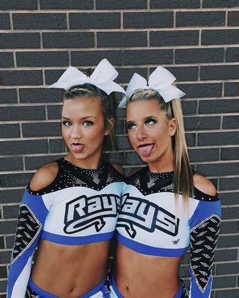 Two Cheerleaders Posing For A Photo In Front Of A Brick Wall