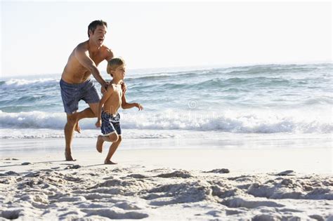 Father And Son Running Along Beach Together Wearing