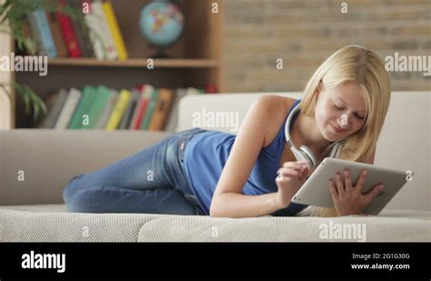 Attractive Girl Wearing Headset Lying On Couch Using Touchpad Looking