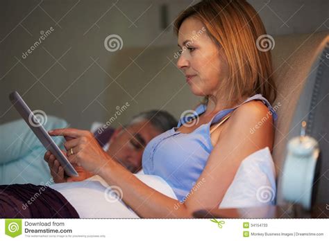 middle aged couple in bed with woman using tablet computer