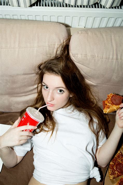 a woman laying on the couch drinking from a red cup and eating pizza