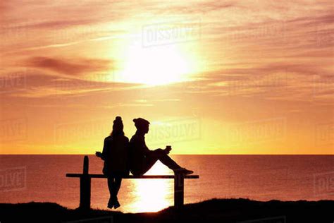 silhouette of couple sitting on bench and drinking tea from thermos